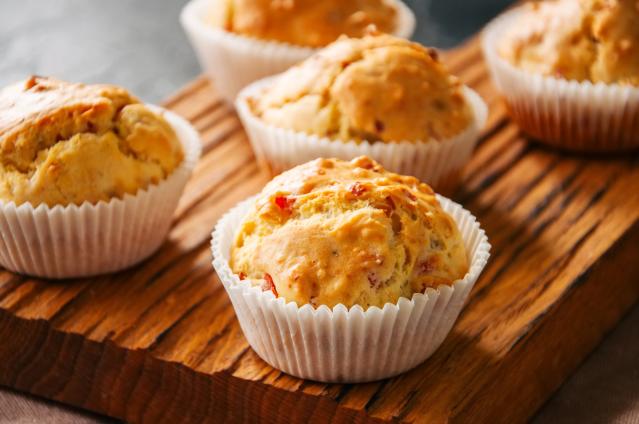 Savoury muffins in white paper cases on a wooden board, with visible pieces of ham and cheese baked into the muffins.