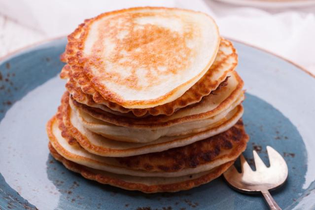 A stack of small golden-brown apple and cinnamon pancakes on a blue plate, showing lightly crisp edges and a fluffy texture. A small fork rests beside the pancakes.