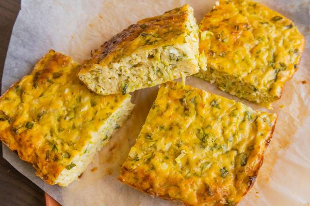 Four square pieces of baked frittata on baking paper, showing a golden-brown surface and a fluffy interior with visible green herbs and vegetables.