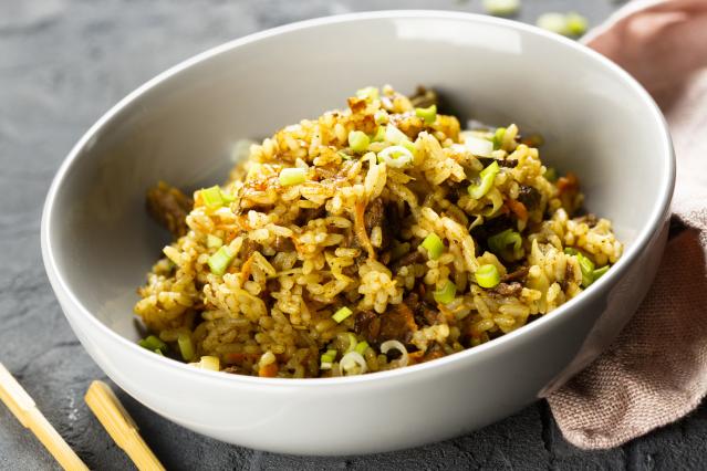 A bowl of chilli and ginger mince stir-fry served over rice. The dish contains seasoned minced meat, vegetables, and rice, topped with sliced spring onions. Chopsticks and a folded cloth sit beside the bowl.