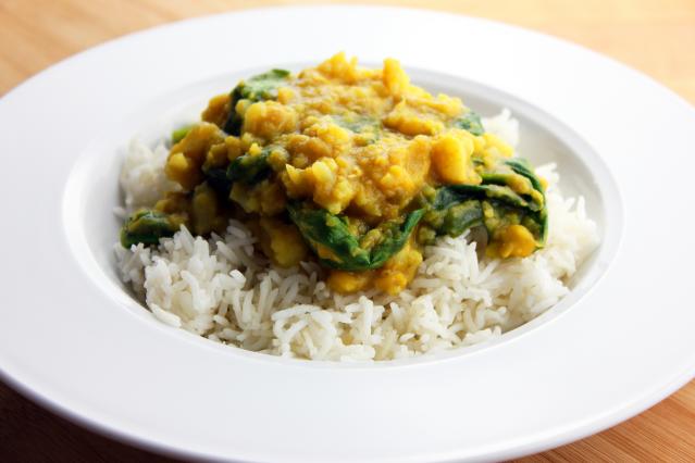 A bowl of dhal curry with cauliflower and spinach served over white rice. The golden-yellow lentil curry contains pieces of cauliflower and wilted spinach and is spooned onto a bed of fluffy rice in a white bowl.