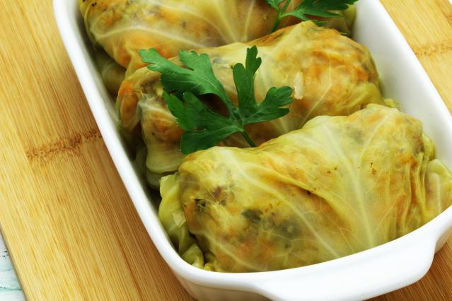 A white baking dish containing several oven-style hāngī parcels wrapped in pale green cabbage leaves. The cabbage leaves are folded around a filling of meat and vegetables, with carrot visible through the translucent leaves.