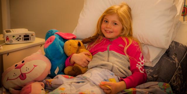 Young girl around 8 years of age lying in a hospital bed with her toys waiting to have an overnight oximetry test