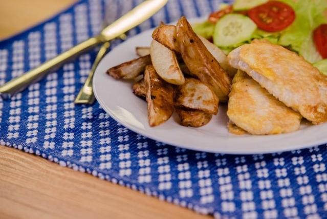 Grilled fish fillet served with potato wedges, lettuce, tomato and radish salad, and a slice of lemon on a white plate.