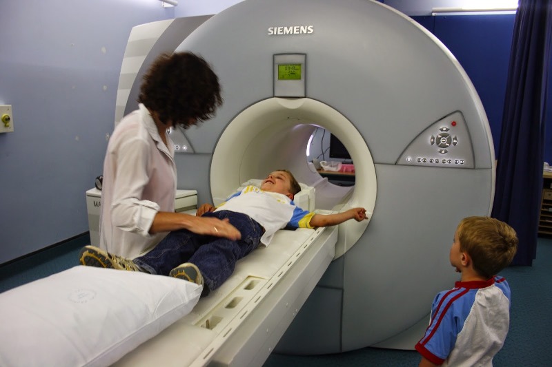 Child going into MRI scanner with radiologist standing over child and sibling looking on