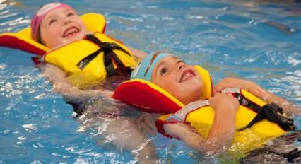 Two young children swimming in a pool wearing lifejackets