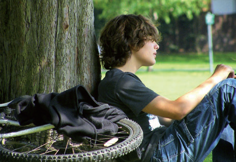A teenage boy sitting against a tree