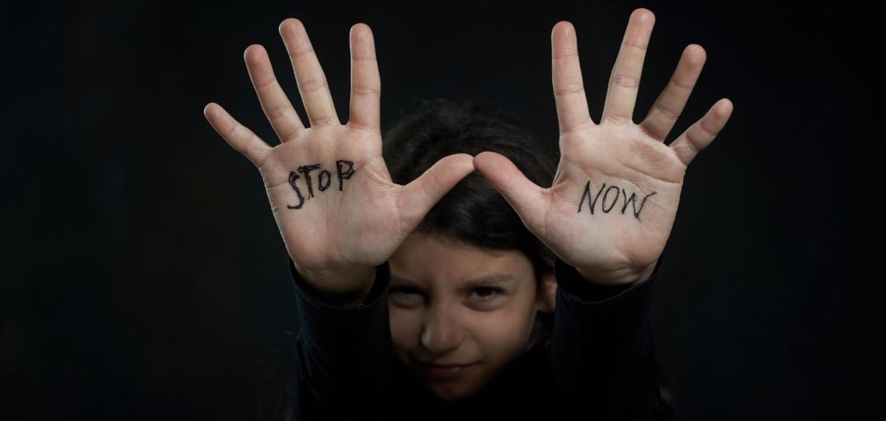 Photo of a young child holding up both hands - hands have the words 'stop' and 'now' written on the palms of each hand