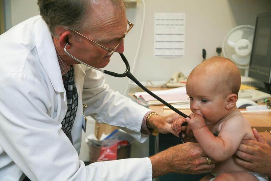 Doctor examining baby with a stethoscope, parent's hands visible holding baby