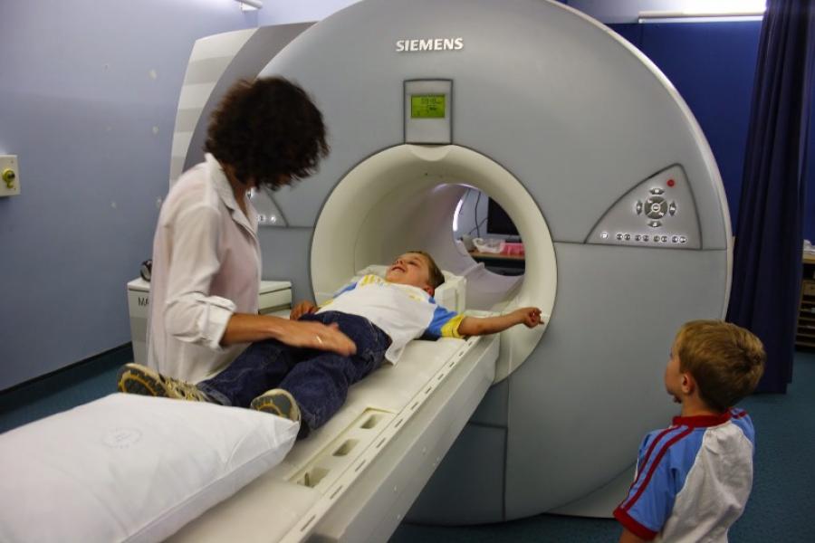 Child going into MRI scanner with radiologist standing over child and sibling looking on