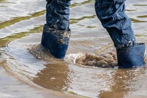 A person's legs with gumboots shown walking through flooding