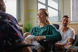 Mum holding baby talking to a health professional with father and support person looking on